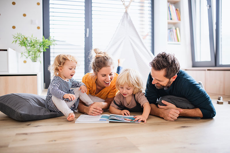 Family of 4 laying on the floor, reading a book